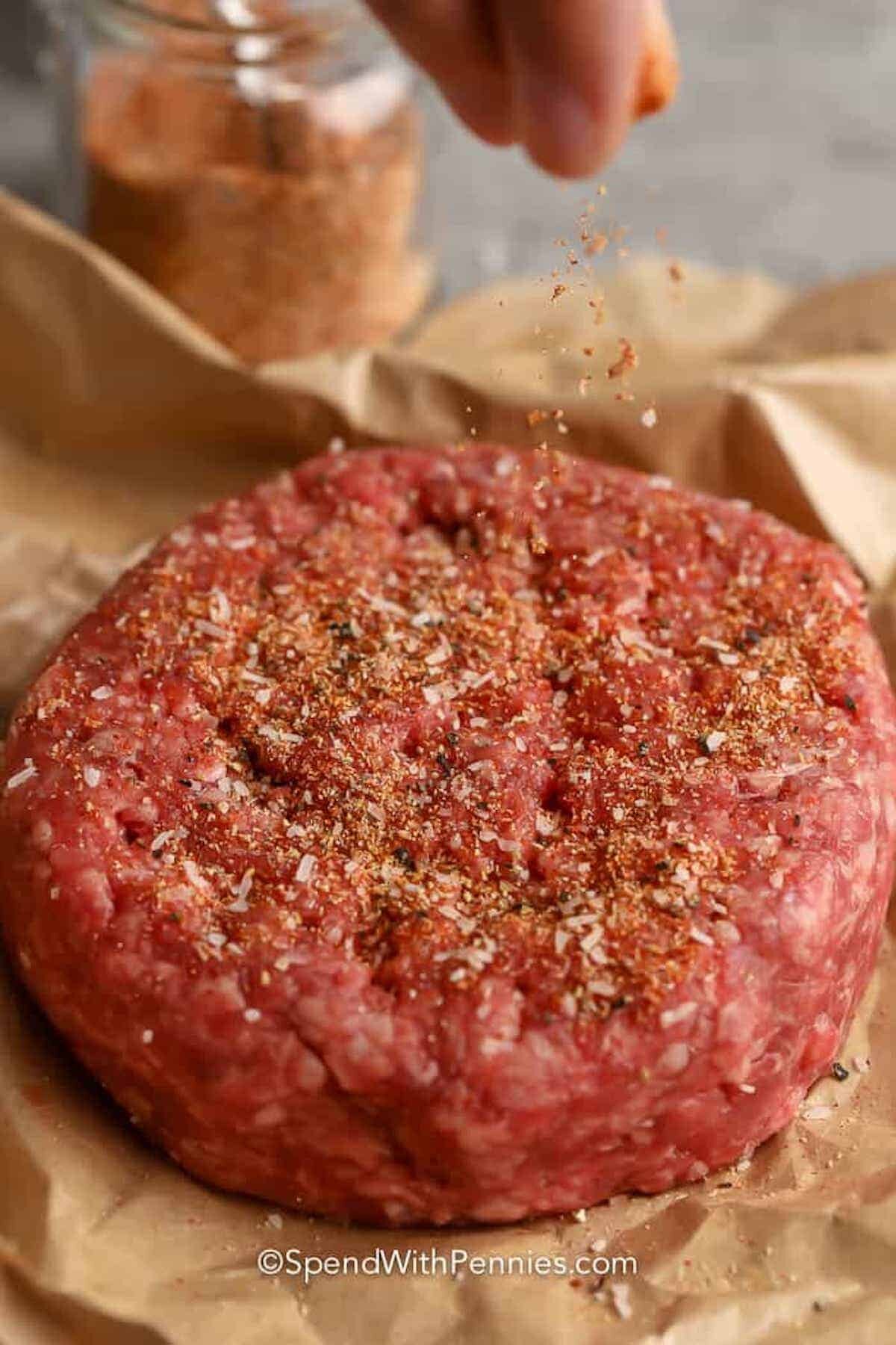 hamburger seasoning being sprinkled on a raw hamburger patty