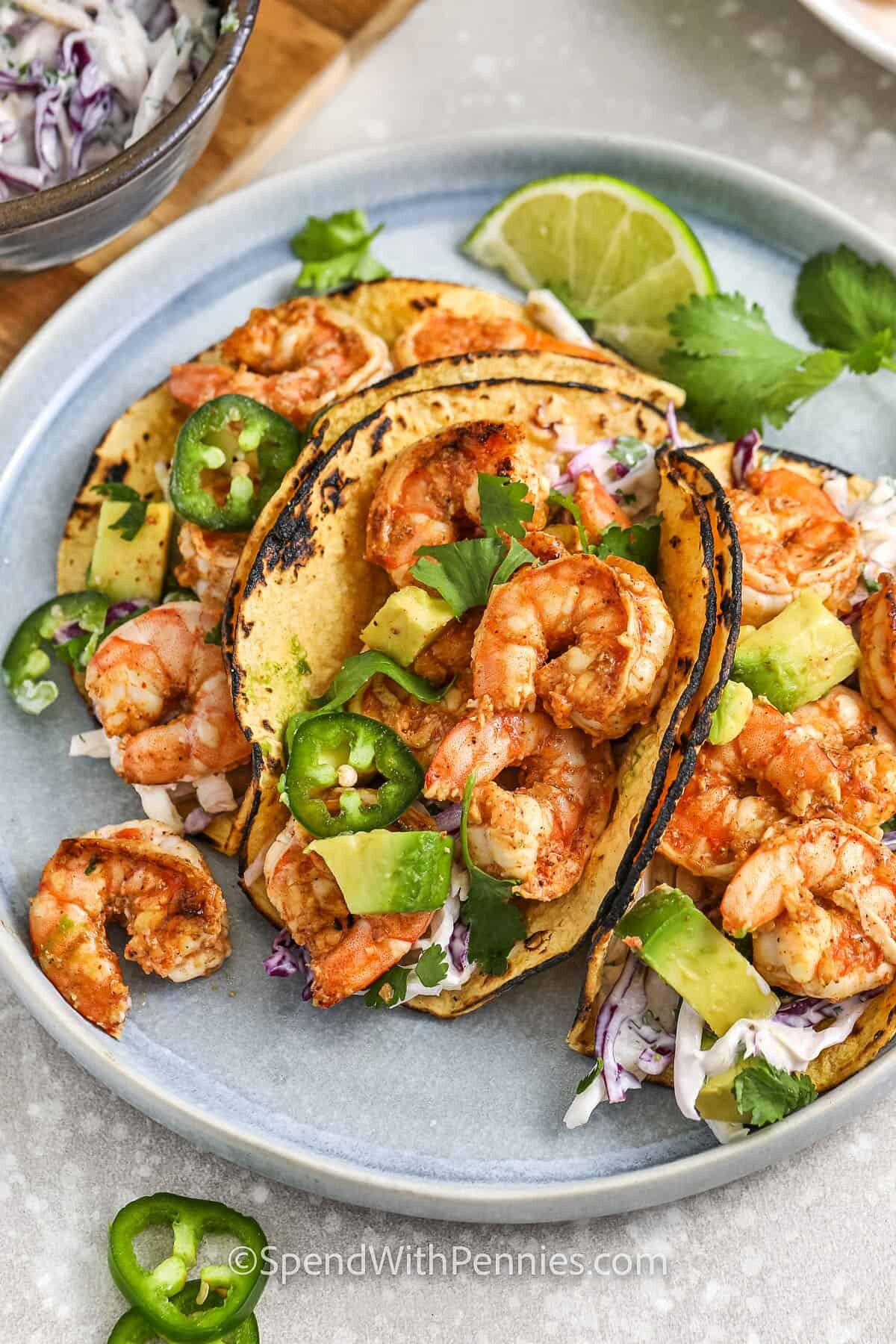 A plate of shrimp tacos topped with jalapenos, avocados, cilantro, and limes